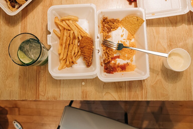 top down view of fries, fried chicken, rice and chips in a styrofoam take out container left on the table
