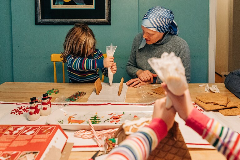 family works together during a christmasy photo session to build gingerbread houses 