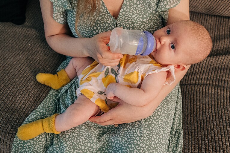 mother holds baby drinking a bottle while family is moving on from this city