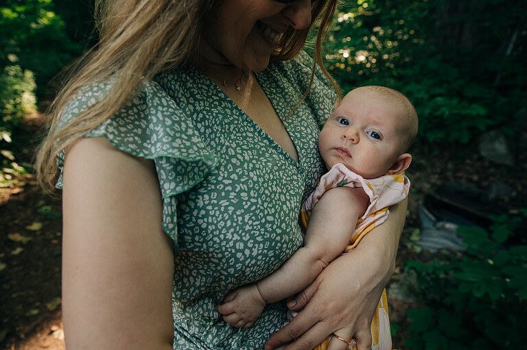 baby girl held by mother in a green dress while walking in a forest of dappled light