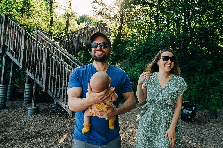 mom and dad smiling and laughing at the beach holding their baby. they will be moving on from this location