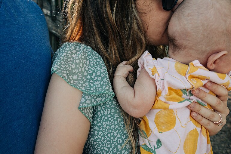 tight shot of mom holding baby wearing lemon onesie, mom in green dress, and dad in blue shirt. Baby holding a fistful of mom's hair