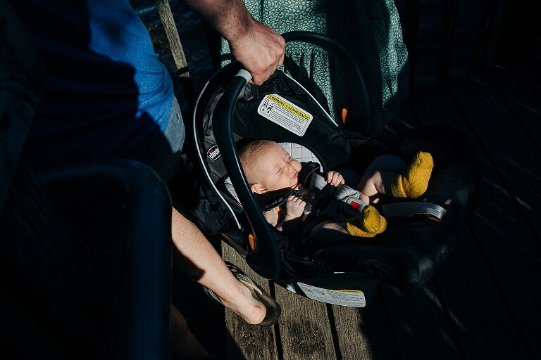 baby in a car seat is highlighted by sunshine as a parent carries the car seat 