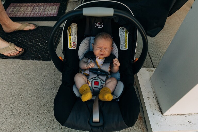 baby sneezes as car seat sits outside in the sunshine while family is moving on