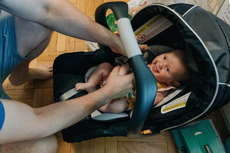 baby smiles huge while father buckles car seat