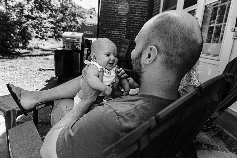 black and white. baby smiles at dad on back porch while family prepares to be moving on from this home