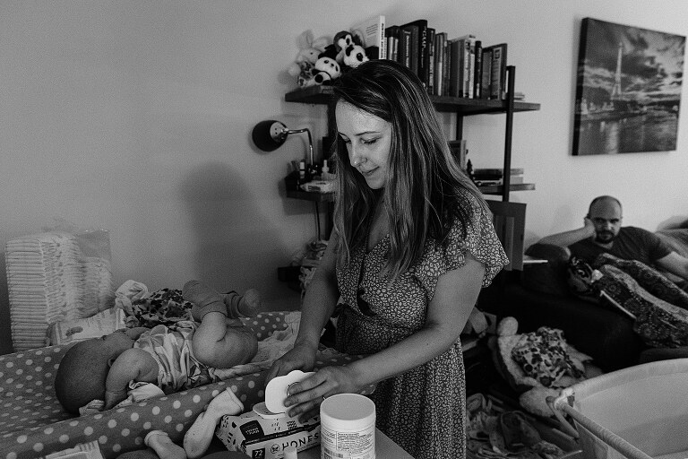 mother changes baby's diaper while dad looks on from the couch in a home they will be moving on from
