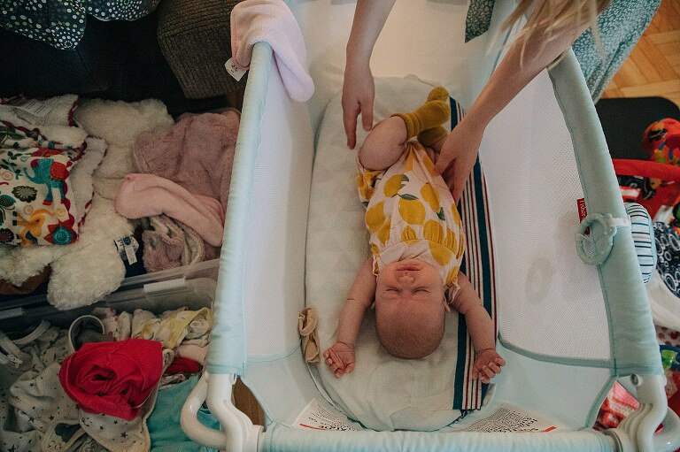 baby stretches in a basinet while mother lays baby into it