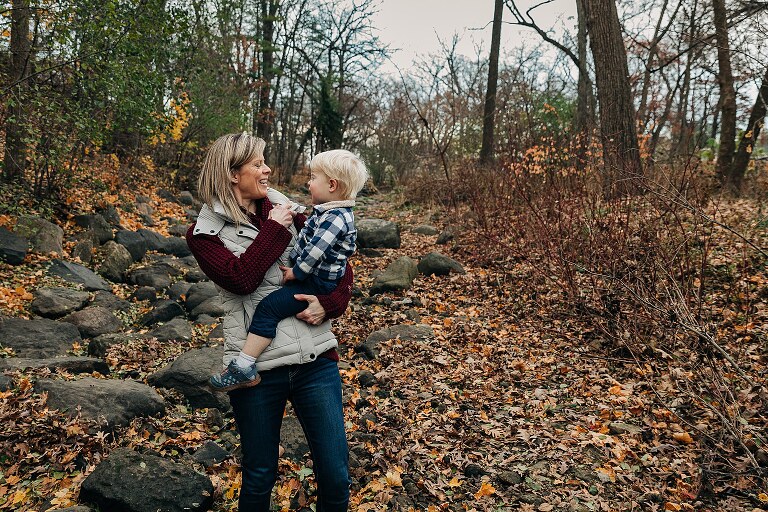 mom holds toddler in a creek bed in the late fall together 
