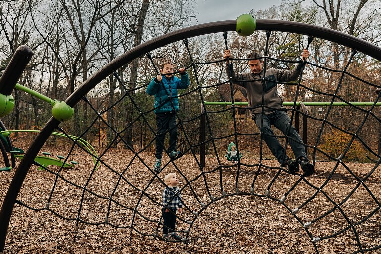dad and three boys visible on a web-like play structure at the park together