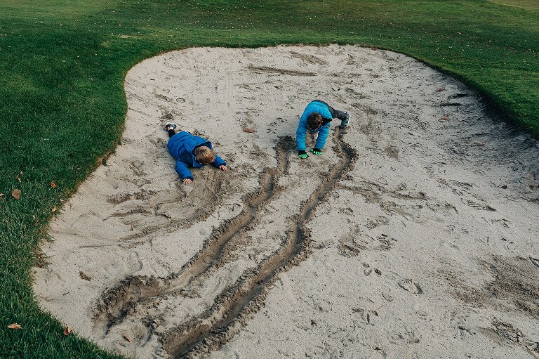 two boys in blue coats make stripes in the sand together