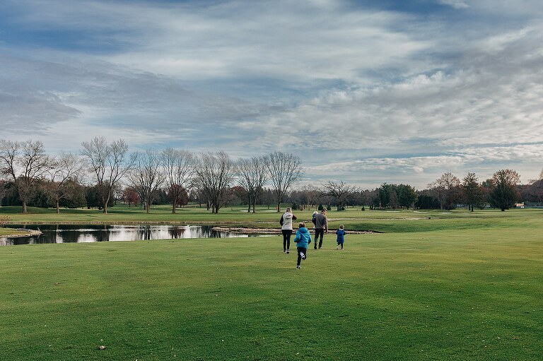 family of 5 runs across golf course under late fall skies together