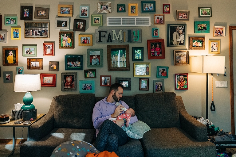 father feeds newborn on couch with many pictures above them