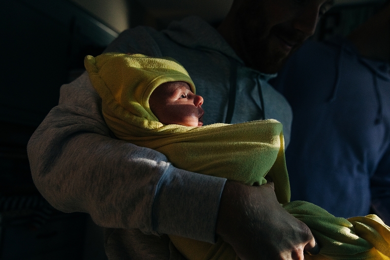 Newborn swaddled in yellow blanket being held by father
