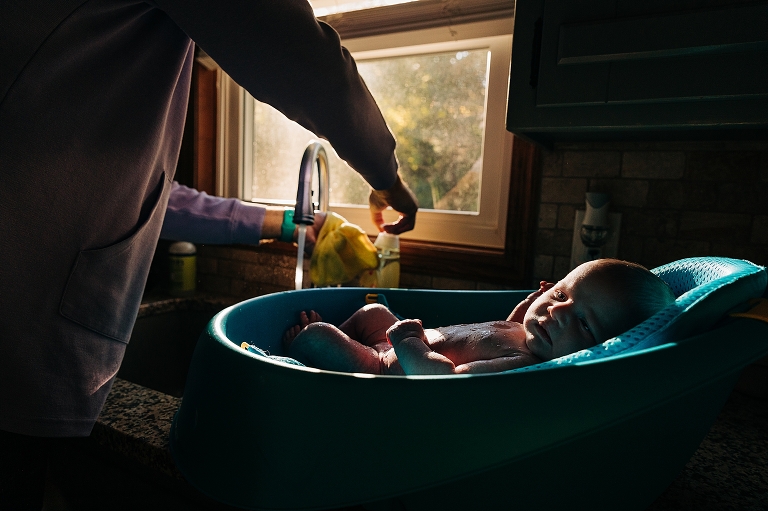 Newborn baby lies in aqua cradle after bath as parent washes rag.