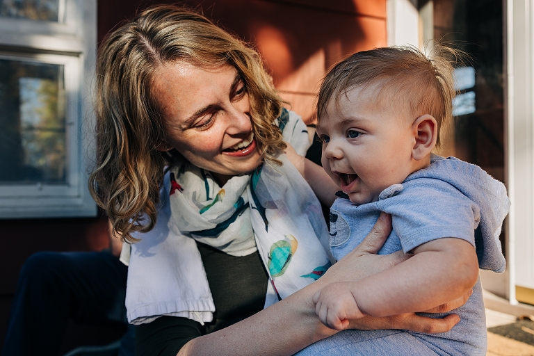 mothers hold infant son, both smiling, in beautiful natural light 