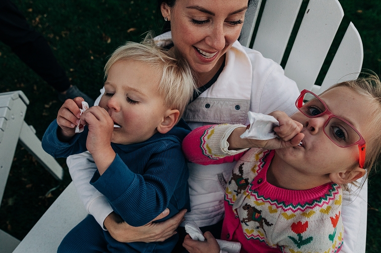 two kids sit on mothers lap eating popsicles
