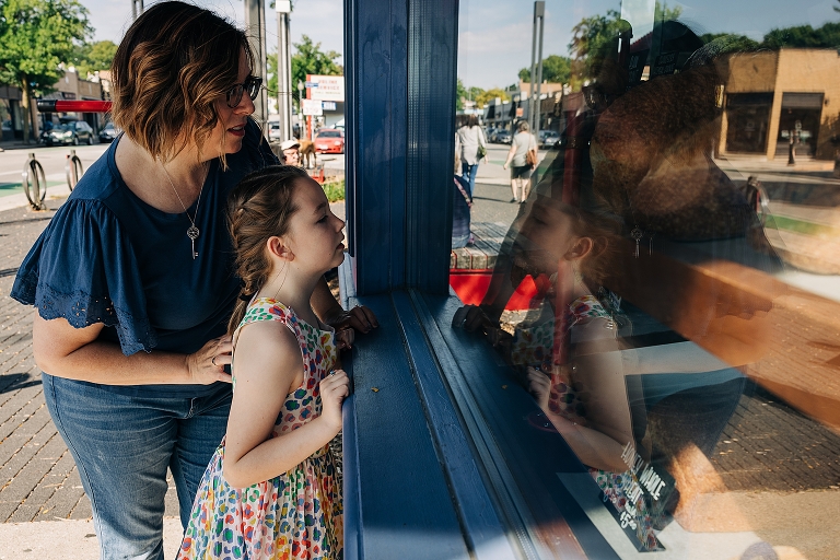 mothers and daughter look in bakery window, reflection is present 