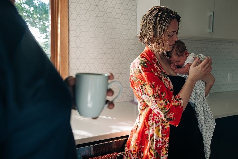 coffee cup in foreground, mothers holding newborn son in background