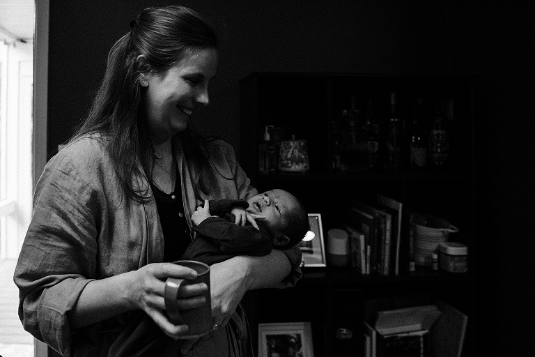 Mothers hold a coffee mug in one hand and newborn child in the other 