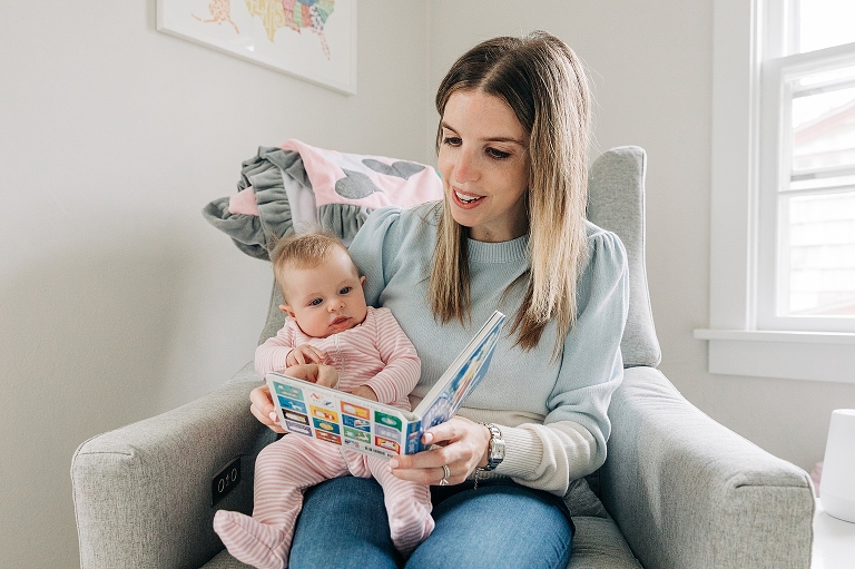 mothers hold infant child on lap on a rocking chair while reading a board book