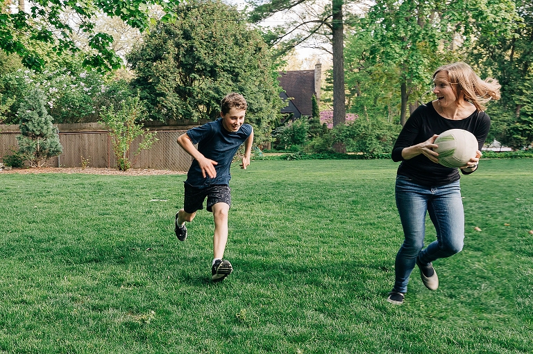 mothers run next to teen son while holding a ball and running; playing kickball