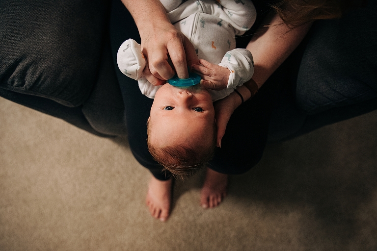 Mom holds pacifier in newborn's mouth with soft ambient light illuminating the side of the frame