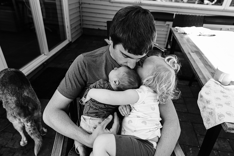 Dad, daughter, and newborn embrace on the patio
