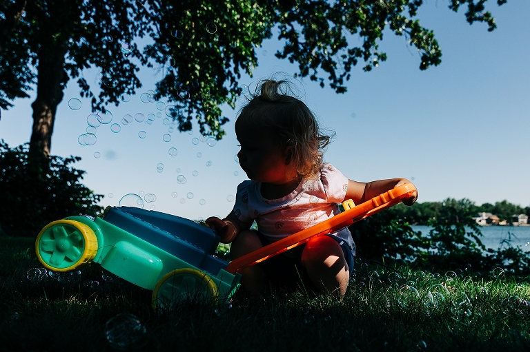 colorful picture of girl examining bubbles coming out of a toy lawn mower on the lake 