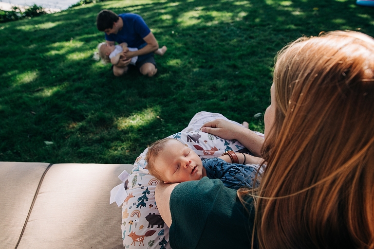 Mom and newborn are in the foreground, and dad and toddler daughter are in the background in a similar position. 