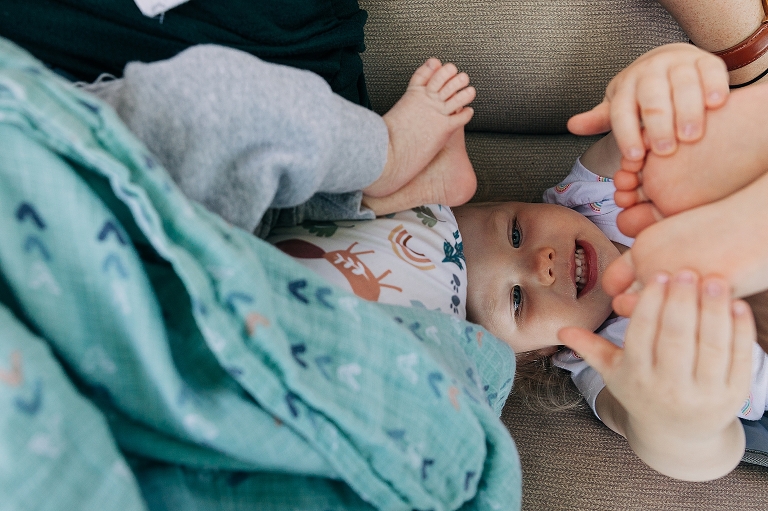The toddler girl examines her own feet while her brother's are above her. 