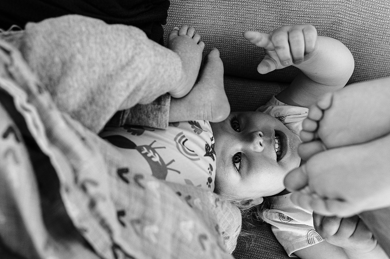 Toddler girl points out her newborn brother's feet while holding up her own.