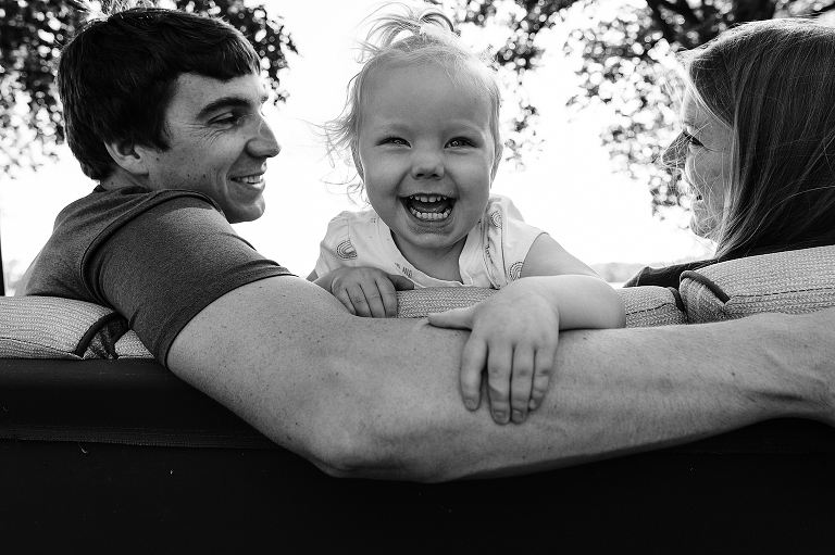 Joyful, happy toddler daughter smiles at camera while framed by her parents looking at each other 