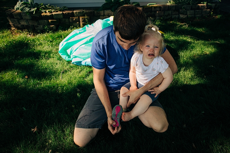 Toddler girl cries while dad puts shoes on her. 