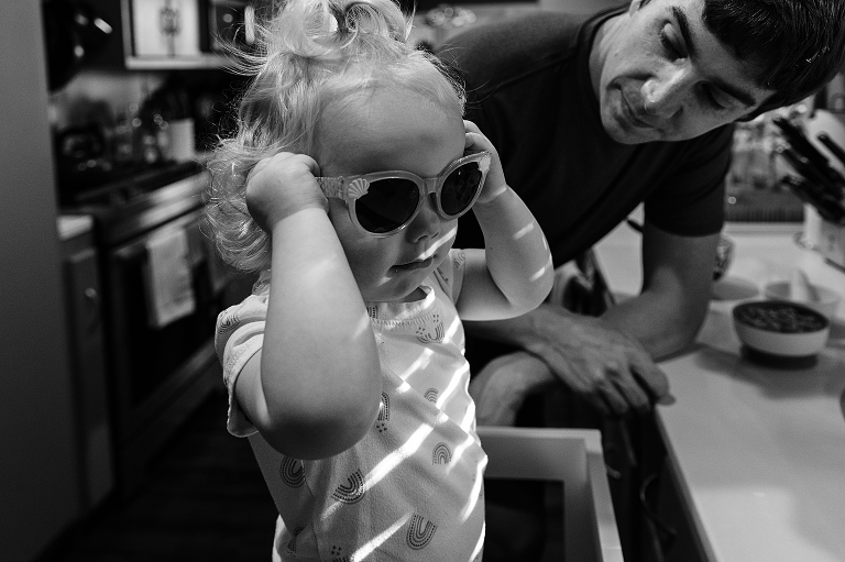 toddler girl tries on sunglasses while dad look on