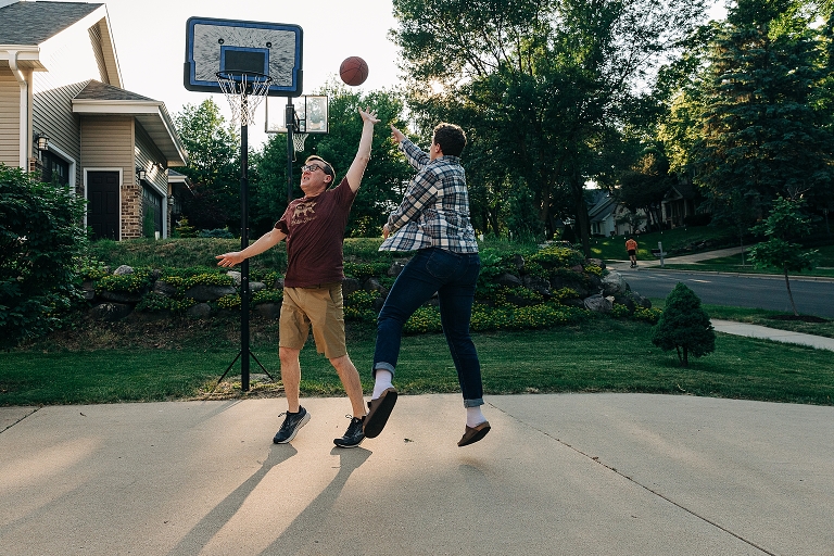 Eldest son attempts one arm contested floater with father in defense on outdoor basketball hoop