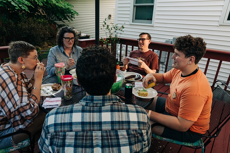 Family member eat, laugh, and converse at grill dinner on patio, "all together now"