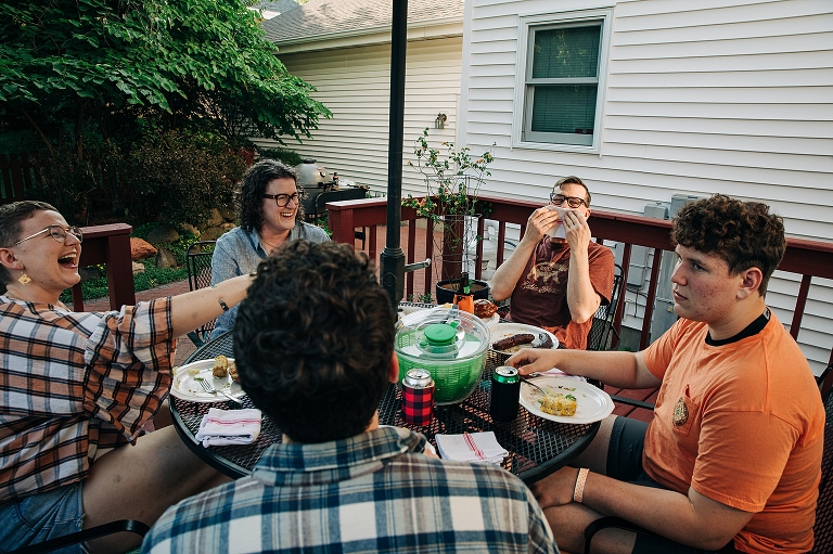 Family members all laugh at serious faced youngest brother during their meal