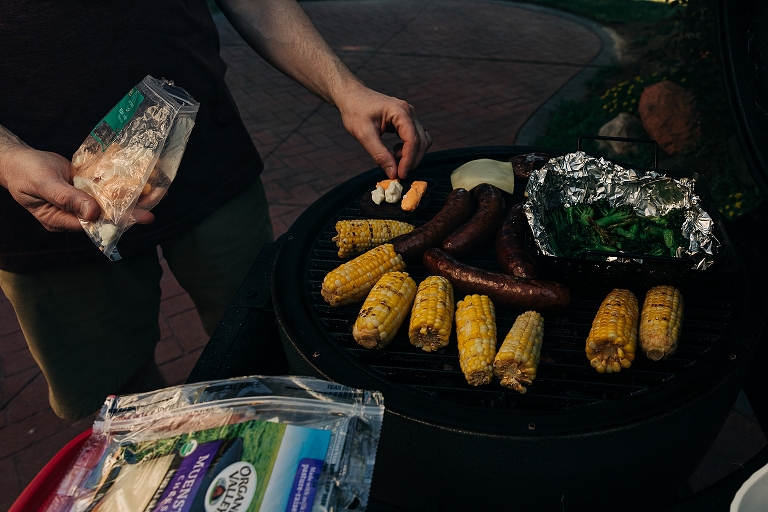 Father arranges "grill charcuterie" with grilled bratwurst, cheeseburgers, grilled corn on the cob, grilled asparagus and cheese curds 