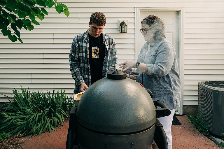 Adult son helps his mother take sausages on the grill 