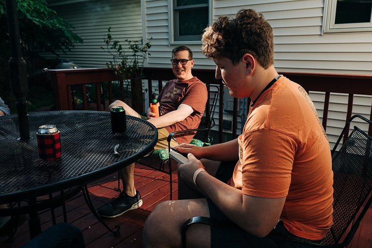 Younger adult son widdles wood with pocket knife at the unset dinner table as dad observes 