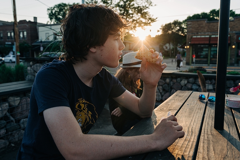 Eldest son looks into his empty ice cream cone as the setting sun blazes orange in background