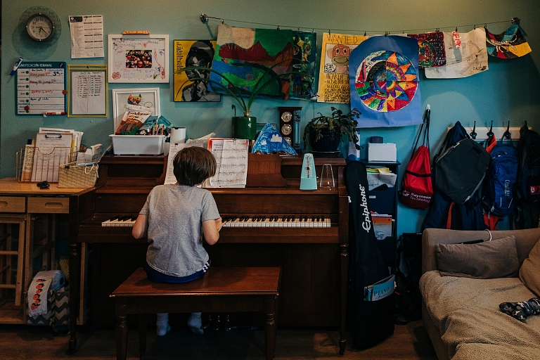 Wide Shot: youngest son plays piano in his room covered in his art