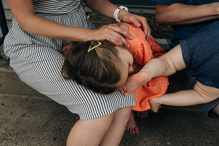 Daughter in orange dress lays on mother's (in striped dress) lap 