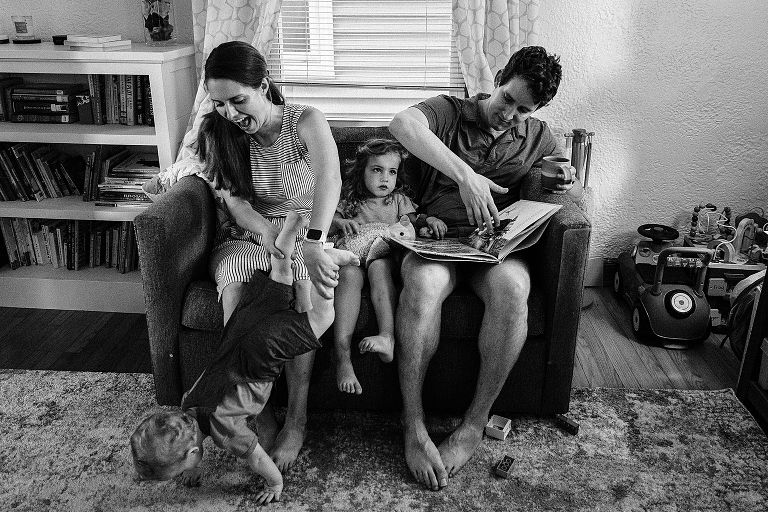 Black and white: mother, daughter and father read a book on the coach as the son plays with his mother