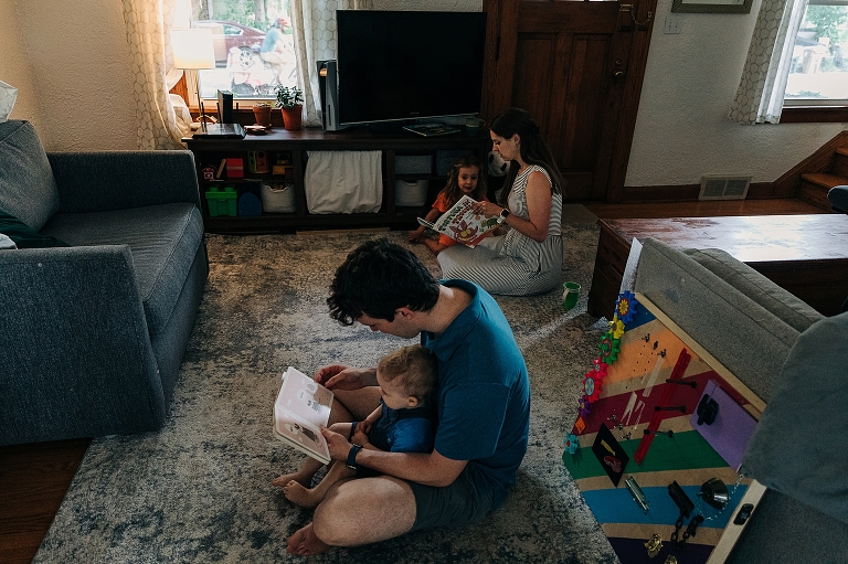 Father reads to son, while mother reads to daughter in living room of home 