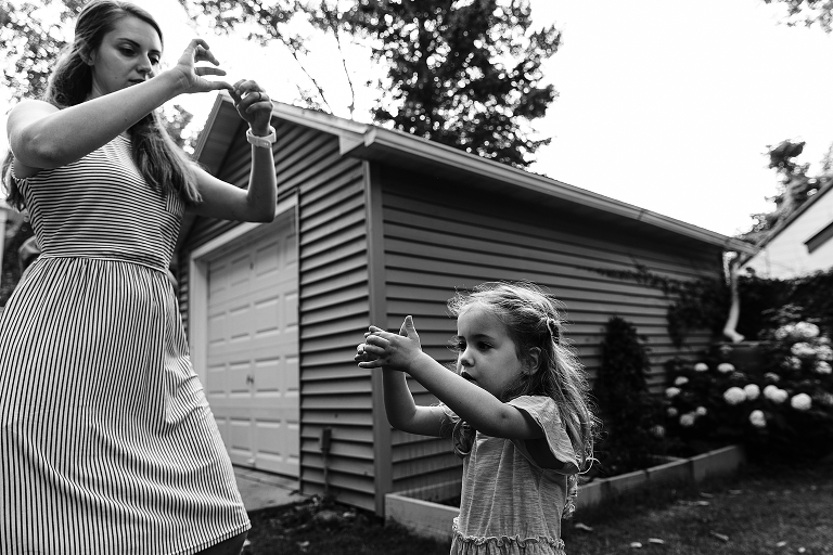 Black and White: Mother and daughter practice "shadow puppets" during evening with a garage in the background