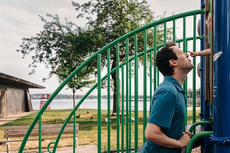 Son touches father's nose while standing on a play structure at Tenney Park. 