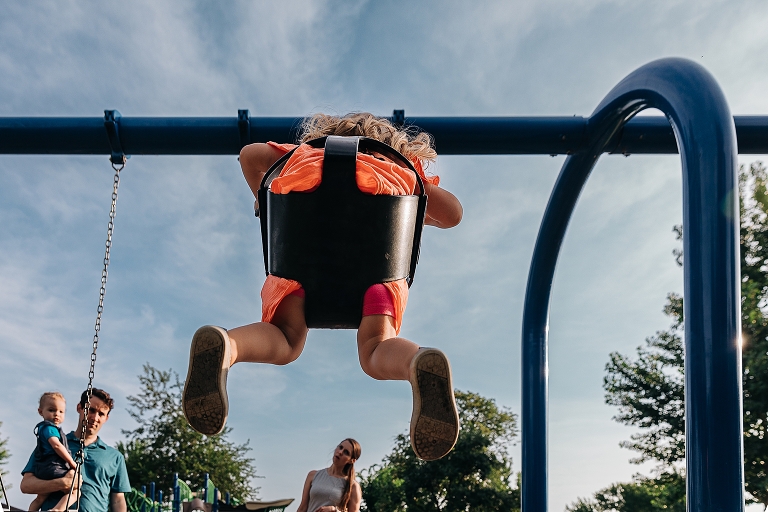 Undershot: daughter on swing at Tenney Park with the rest of the family in the background