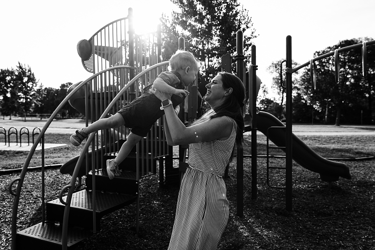 Black and White: Mother playfully lifts up son with playground in background at Tenney Park